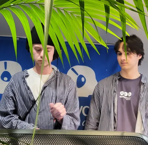 Deux jeunes derrière une palme, devant un fond bleu