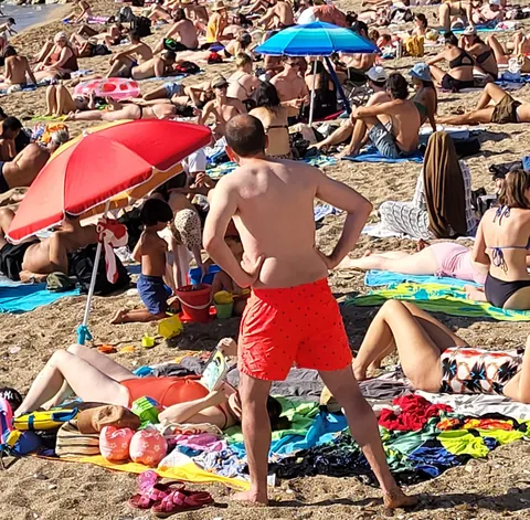 Un homme en maillot rouge debout au milieu d’une plage noire de monde