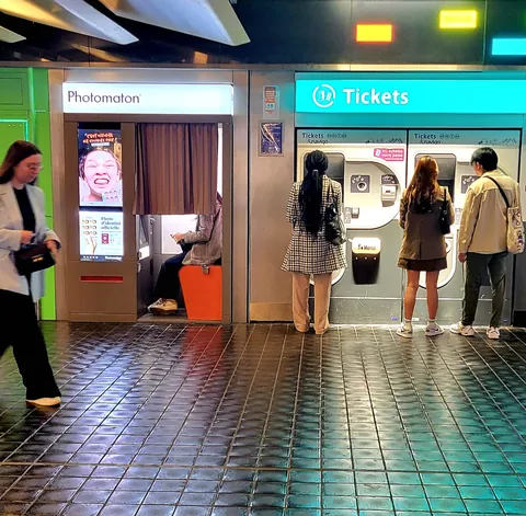Des voyageurs devant les automates à tickets et le photomaton