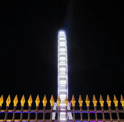 Une grande roue illuminée derrière une grille aux pointes dorées