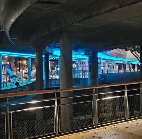 Un train bleu illuminé sous un pont, la nuit