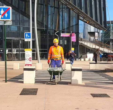 Un ouvrier en orange pousse une brouette sous un panneau de sens interdit