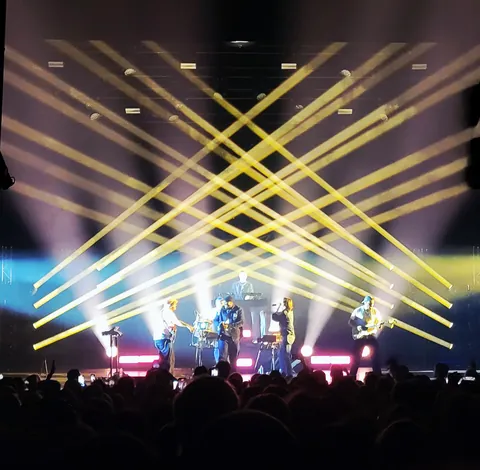 Un concert, des faisceaux de lumière jaune qui se croisent au-dessus de la scène