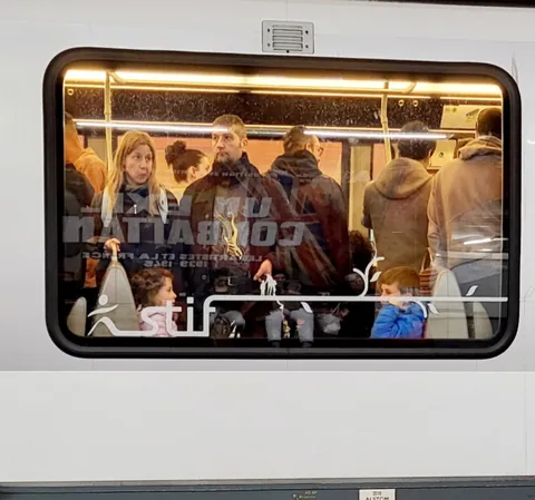 Des voyageurs serrés dans un wagon, vus à travers la fenêtre d’un train
