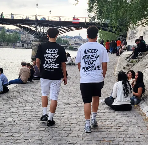 Deux garçons de dos en t-shirts « Need money for Porsche » sur les quais de Seine