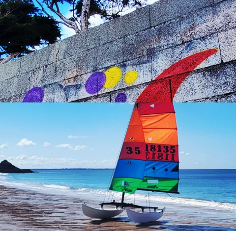 Un catamaran à voile multicolore échoué sur une plage, sous une fresque