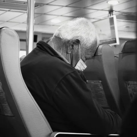 Un homme assis dans les transports dort avec le front appuyé sur le siège devant lui