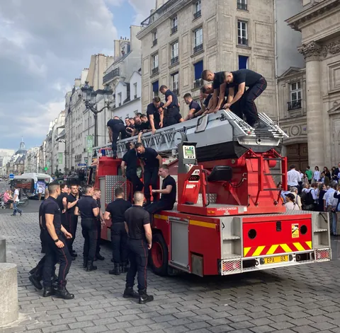 Des pompiers juchés sur leur camion rouge dans une rue