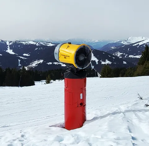 Un canon à neige jaune et rouge sur une piste, comme un sèche-cheveux géant
