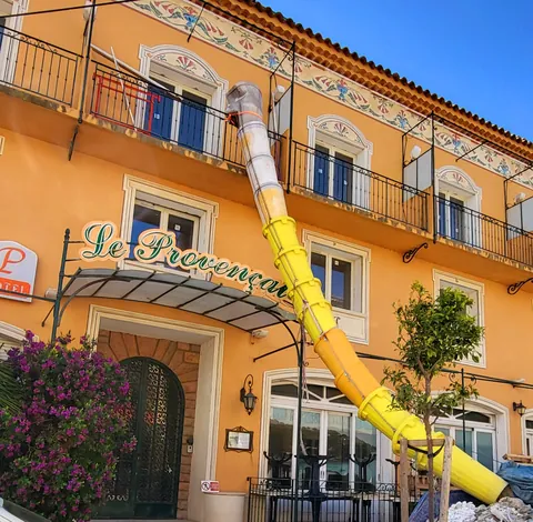 Un toboggan jaune qui sort de la façade d’un hôtel, comme une trompe