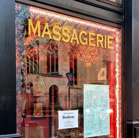 La vitrine d’un salon de massage, « Massagerie » en lettres dorées, où se reflètent les façades d’en face