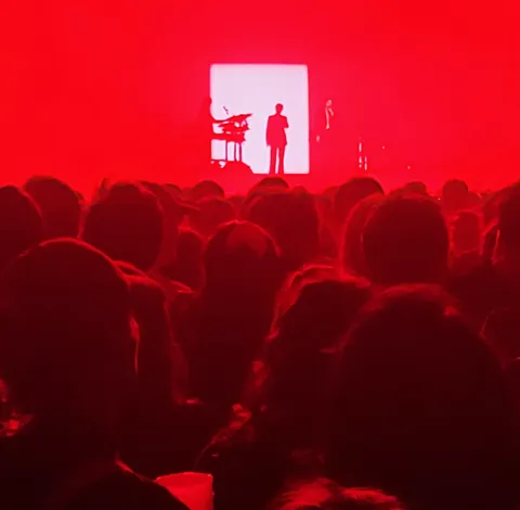 Une salle de concert baignée de lumière rouge, un musicien en silhouette