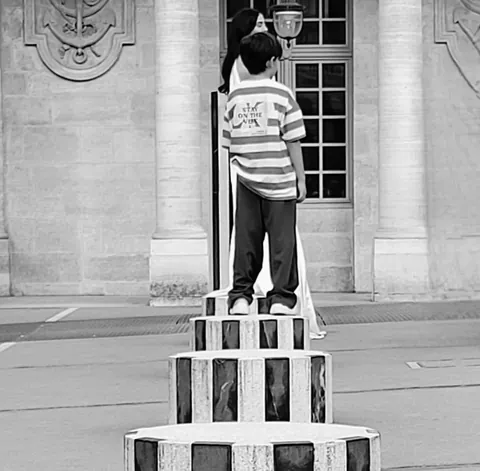 Un enfant en noir et blanc debout sur une colonne rayée de Buren