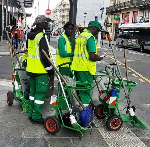 Trois agents de propreté en gilet jaune fluo avec leurs chariots verts, au bord d’un trottoir