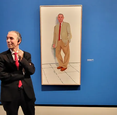 Un homme en costume pose devant son propre portrait au musée