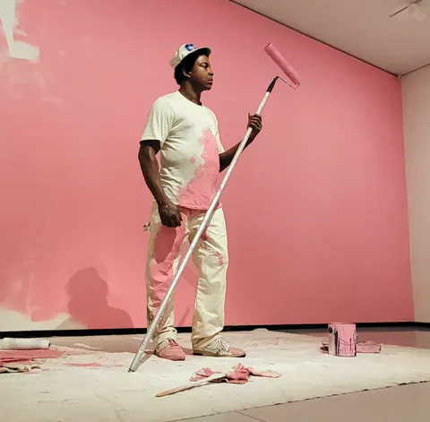 Un peintre en blanc devant un mur rose fraîchement peint