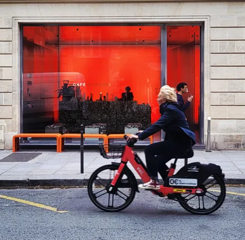 Une cycliste qui passe devant une vitrine rouge de café