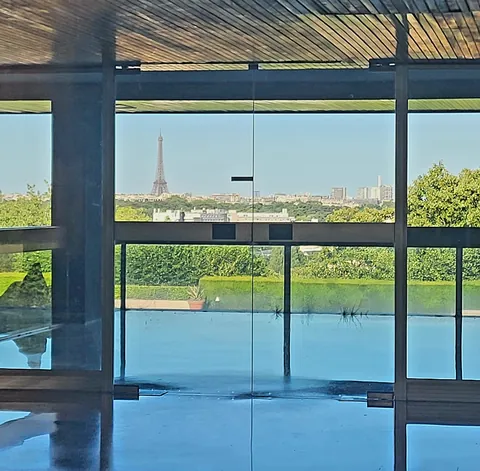 La tour Eiffel au loin, vue à travers la baie vitrée d’un hall au-dessus d’un bassin