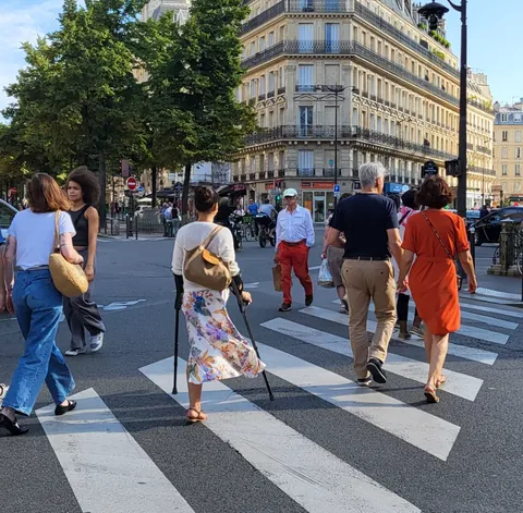 Des passants qui traversent un passage piéton, dont une femme avec une canne