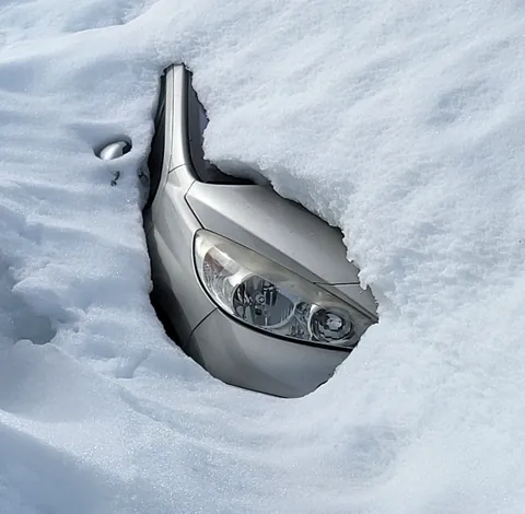 Une voiture grise presque entièrement enfouie sous la neige