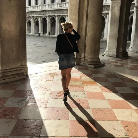 Une femme marche entre les colonnes d’une galerie illuminée par le soleil