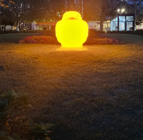 Une lampe jaune lumineuse en forme de tête posée sur une pelouse, le soir