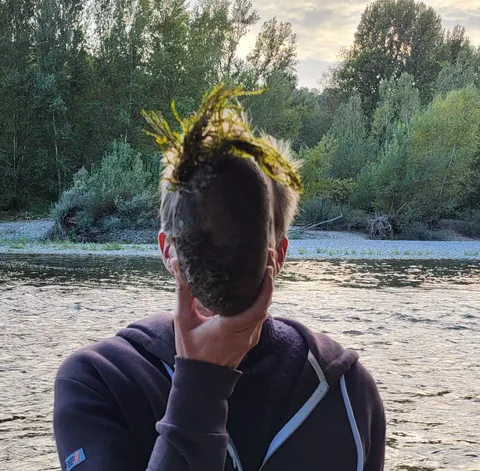 Un homme qui se cache le visage de la main, devant une rivière bordée d’arbres