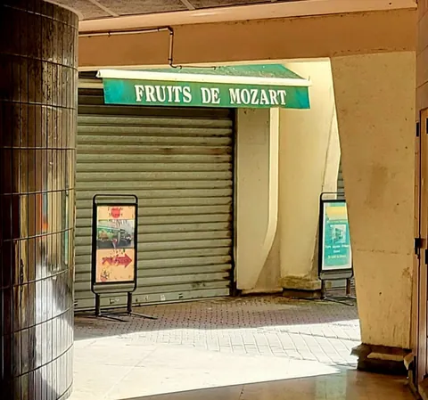 Une boutique au rideau baissé sous l’enseigne verte « Fruits de Mozart », dans un passage