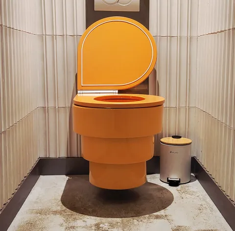 Des toilettes orange suspendues au milieu d’une cabine