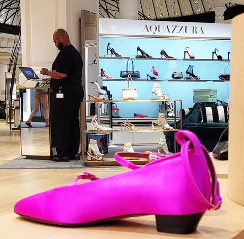 Un vendeur dans une boutique de chaussures, une énorme chaussure rose fuchsia au premier plan