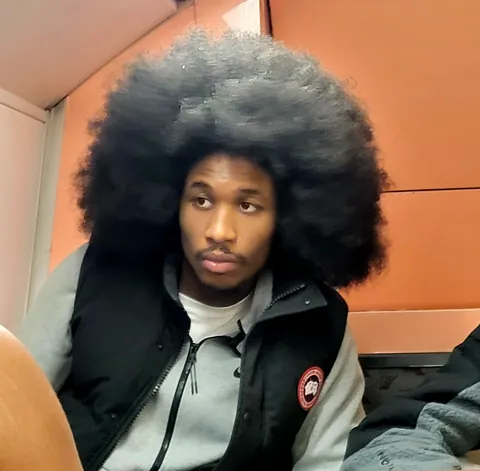 Un jeune homme à l’immense coupe afro, assis dans un train