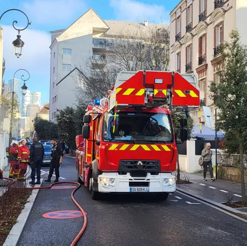 Un camion de pompiers rouge arrêté dans une rue, des pompiers et un tuyau déroulé sur la chaussée