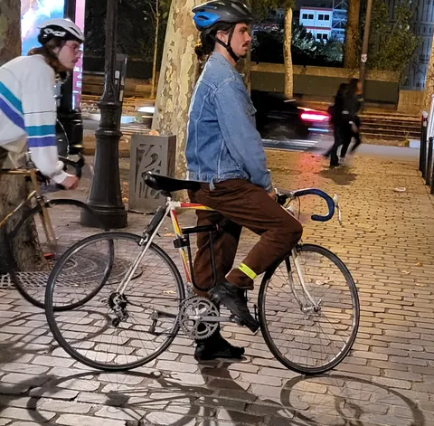 Deux jeunes hommes à vélo, casque sur la tête, sur des pavés mouillés