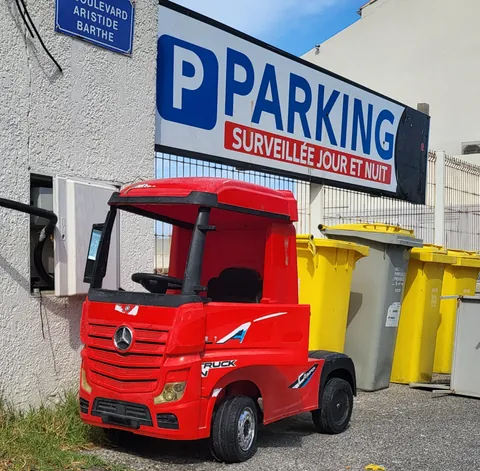 Un camion jouet rouge garé sous un panneau « Parking surveillé jour et nuit »