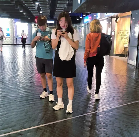 Des jeunes qui marchent dans une galerie, les yeux rivés sur leur téléphone