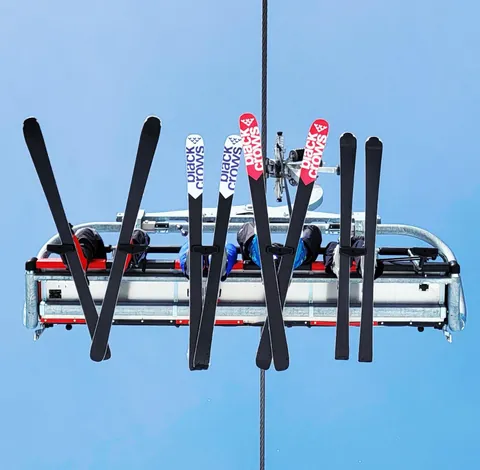 Des skis et des bâtons dressés sous un télésiège, vus d’en dessous