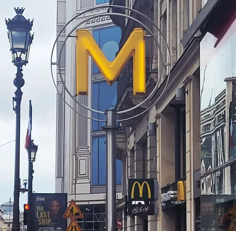 Un grand M jaune de métro devant une enseigne McDonald’s