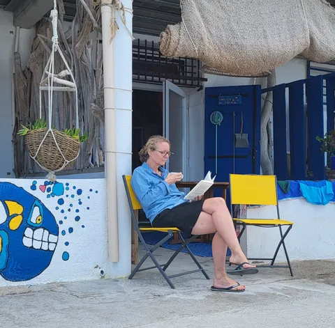 Une femme qui lit sur une chaise pliante, devant une maison de pêcheur