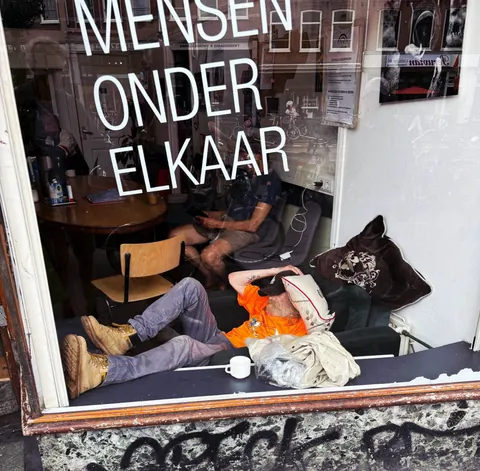 Un homme endormi en vitrine sous l’inscription « Mensen onder elkaar »