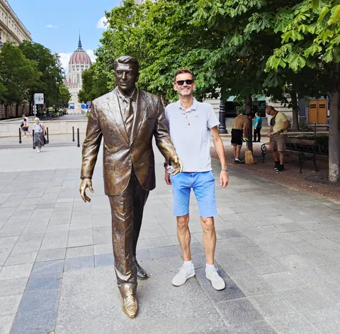 Un homme pose à côté d’une statue de bronze
