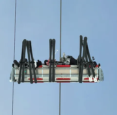 Des skis accrochés sous un télésiège, vus d’en dessous
