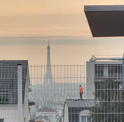 La tour Eiffel au loin, un ouvrier en orange sur un toit au premier plan