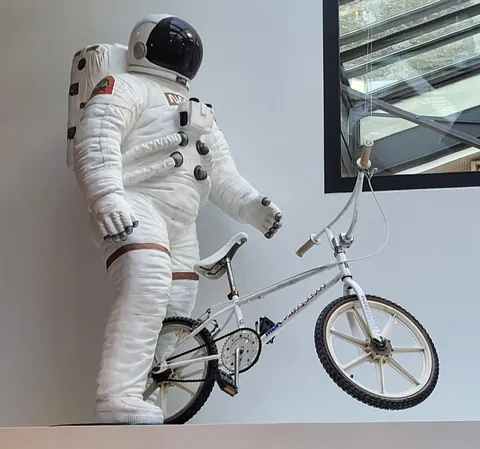 Une statue d’astronaute en combinaison blanche à côté d’un BMX blanc, sur une étagère