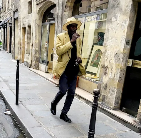 Un homme en veste jaune et chapeau qui marche dans une rue