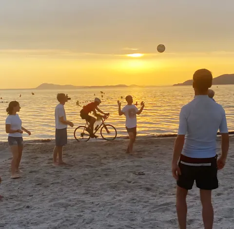 Des joueurs de raquettes et un cycliste sur la plage au coucher du soleil