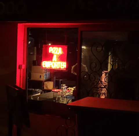 Une enseigne au néon rouge « Pizza à emporter » dans une vitrine, la nuit
