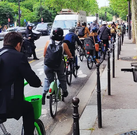 Une file de cyclistes sur une piste cyclable bondée, à côté des voitures