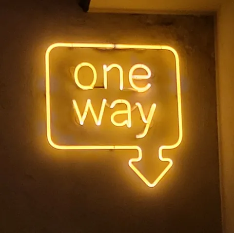Une enseigne au néon jaune « one way », avec une flèche vers le bas