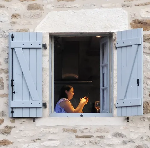 Une femme au téléphone derrière une fenêtre aux volets bleus