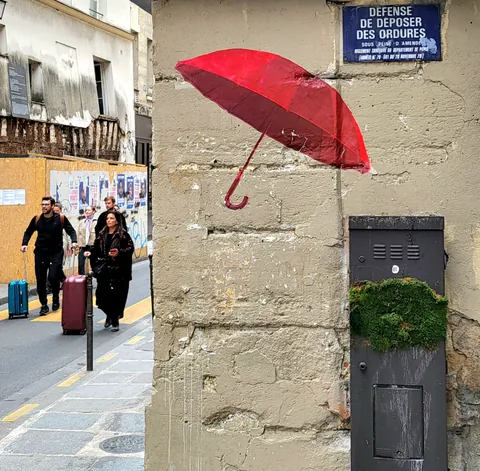 Un parapluie rouge accroché à un mur, sous un panneau « Défense de déposer des ordures »